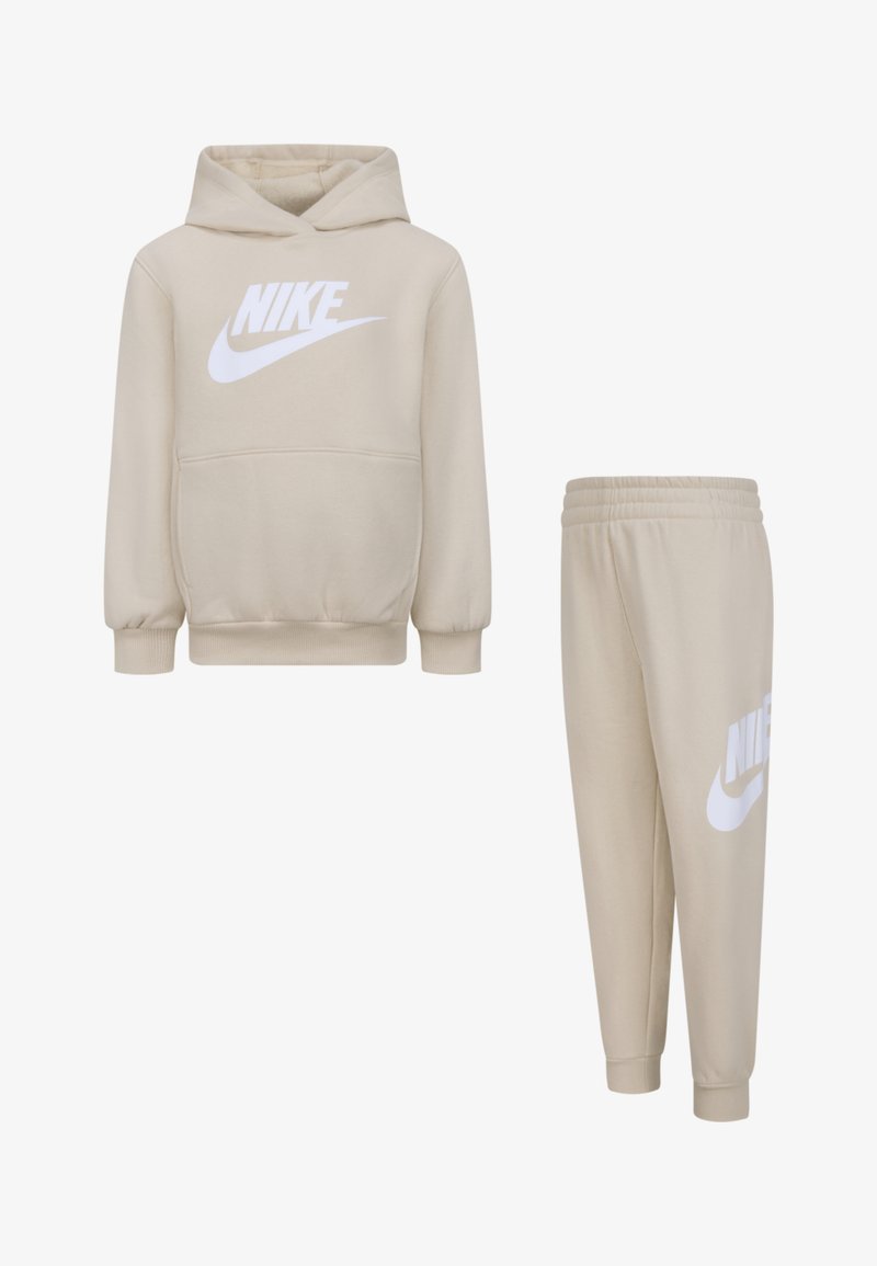 Conjunto de sudadera y pantalones beige. La sudadera cuenta con un bolsillo frontal y el logo de Nike en blanco. Los pantalones tienen una cinturilla elástica y un logo lateral. Textura de tela suave.