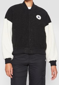 Svart och gräddfärgad bomberjacka i texturerad fleece. Har en ribbad krage och manschetter, knappstängningar och en cirkulär logotyp på bröstet.