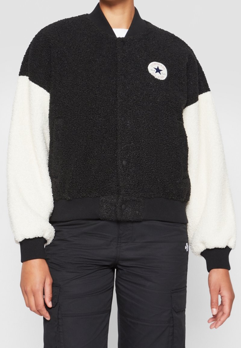 Svart och gräddfärgad bomberjacka i texturerad fleece. Har en ribbad krage och manschetter, knappstängningar och en cirkulär logotyp på bröstet.