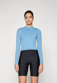 Lyseblå langermet treningstopp med høy hals, sammen med svarte høytlivsykkelshorts. Har logo på brystet.