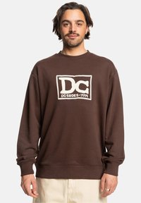 Bruine katoenen sweatshirt met ronde hals, voorzien van een witte DC Shoes-logo in een rechthoekige omtrek. Ribgebreide manchetten en onderkant.