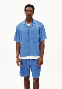 Lichtblauwe denim overhemd met korte mouwen, een kraag, constructie met knopen aan de voorkant en een borstzak; gecombineerd met bijpassende blauwe denim shorts.