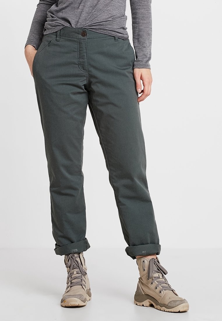 Tummanvihreät puuvillahousut, joissa on suora lahjemuotoilu, käännetyt hihat ja yksi nappikiinnitys. Vaatteena vaaleanbeiget vaelluskengät.