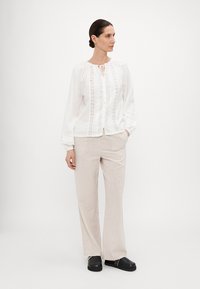 Hvit bluse med broderte detaljer, knappåpning foran og puffede ermer, kombinert med lysebeige vide bukser og svarte klomper.