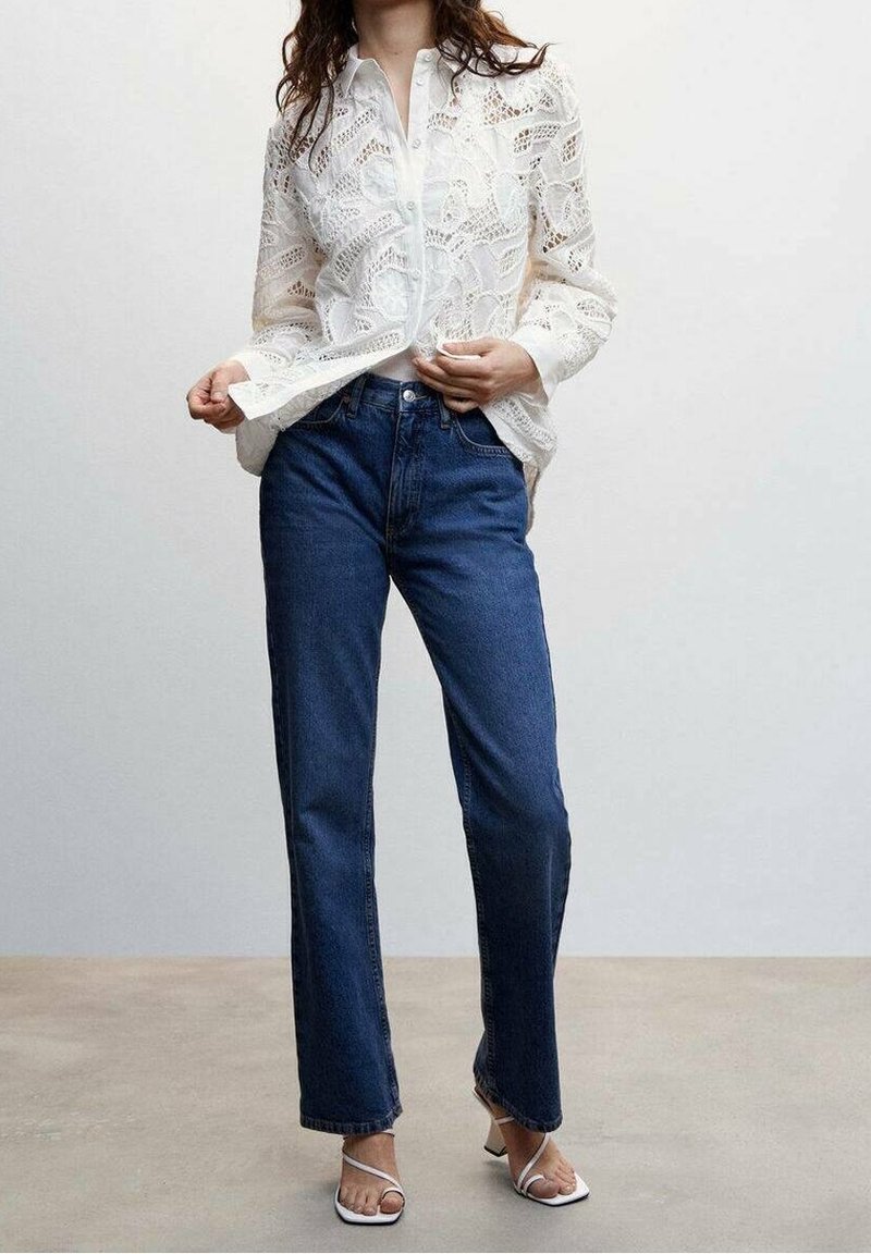 White lace blouse with a button front, paired with classic dark blue straight-leg jeans and white strappy sandals. Smooth textures and intricate patterns.