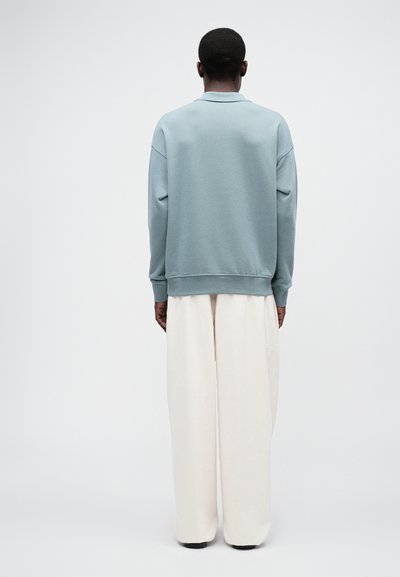 Ljusblå sweatshirt med en avslappnad passform, ribbade ärmslut och rund halsringning, tillsammans med löst sittande krämfärgade byxor. Minimalistisk design.