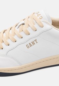 Weißes Leder-Sneaker mit beigen Schnürsenkeln, beiger Sohle und "GANT"-Branding an der Seite, das gestickte Paneeldetails zeigt.