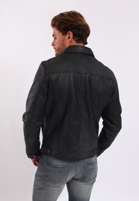 Zwart leren jack met gestructureerde naden, een gekartelde kraag en knopenmanchetten, gecombineerd met lichtblauwe jeans. Glad textuur en strakke lijnen.