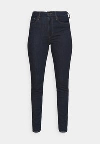 Tmavě modré skinny džíny vyrobené z denimu, s klasickým pětipocketovým designem a hnědými ozdobnými švy.