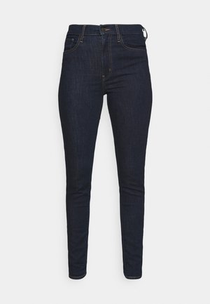 Dark blue skinny jeans made from denim, featuring a classic five-pocket design and brown stitching details on the seams.