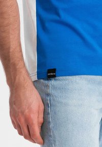 Modrá a bílá polokošile s krátkým rukávem vyrobená z bavlny, s etiketou "ombre" na spodním lemu a volným střihem, v kombinaci se světlými denimovými džíny.