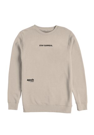 Beige langærmet sweatshirt med sort tekst "STAY SURREAL" centreret på brystet og "apoh London" nær taljen på venstre side.