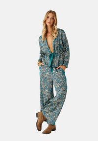 Conjunto de loungewear con estampado floral en tela verde azulado, con escote pronunciado, pantalones de pierna ancha y un cinturón de lazo. Botas marrón hasta el tobillo completan el look.