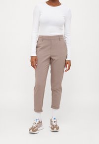 Pantalons beiges légers avec une coupe fuselée, retroussés aux chevilles, associés à un top ajusté à manches longues blanc et des baskets aux tons neutres.