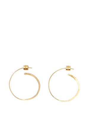 Para cienkich, nieregularnych złotych kolczyków-koła z zapięciami na sztyft, minimalistyczny design i subtelnie wygrawerowana nazwa marki po wewnętrznej stronie.