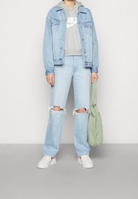 Chaqueta de mezclilla de color azul claro, sudadera gris con logo, jeans de mezclilla azul claro desgastados con rodillas rasgadas, zapatillas blancas, bolso verde de hombro.