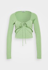 Top verde a maniche lunghe realizzato in materiale testurizzato, con scollatura a barchetta e davanti arricciato con lacci per una vestibilità regolabile.