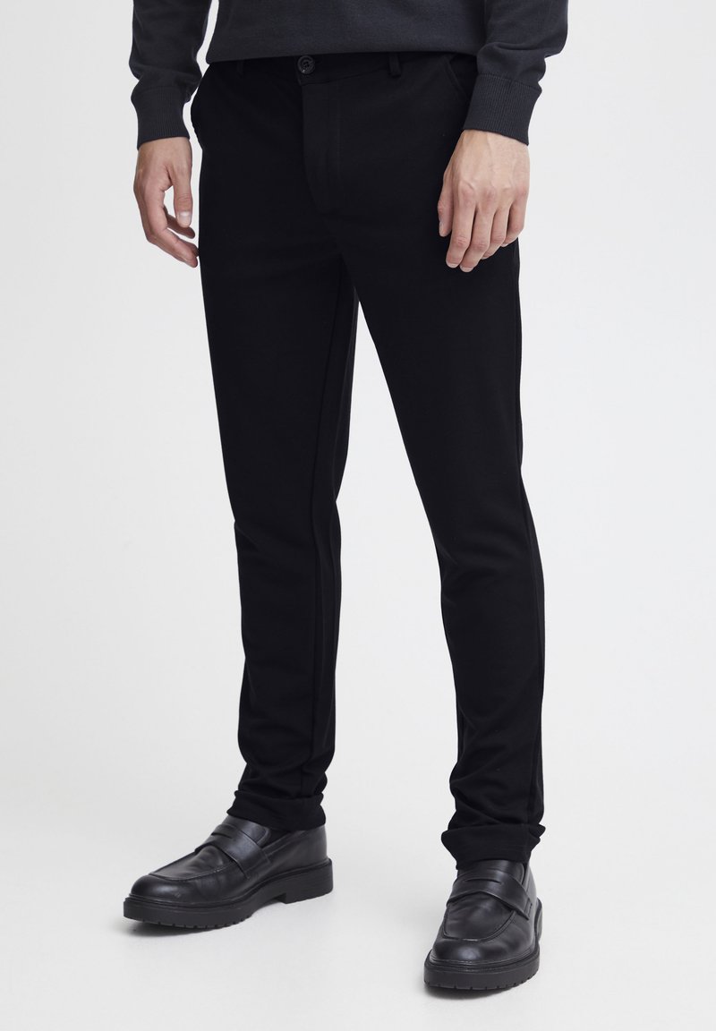 Czarne spodnie o dopasowanym kroju wykonane z gładkiego materiału, z tapered designem i bocznymi kieszeniami, w połączeniu z czarnymi butami typu slip-on.