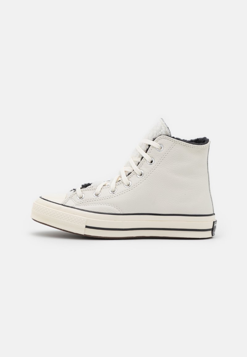 Höga sneakers i vitt läder med en texturerad yta, svart plyschfoder och svarta och vita gummisulor.