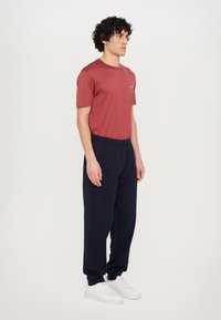 Röd kortärmad t-shirt och marinblå sweatpants, tillverkade av mjukt tyg. Vita sneakers. Enkelt mönster utan synliga mönster eller utsmyckningar.