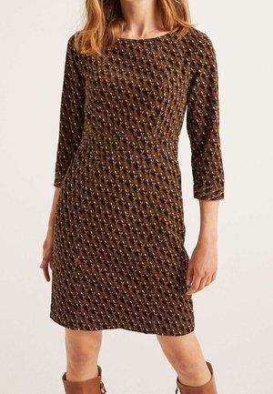 Frau trägt ein knielanges, figurbetontes Kleid mit 3/4-Ärmeln und einem braun-schwarz-beigen geometrischen Muster, kombiniert mit kniehohen braunen Stiefeln.