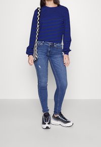 Blue and black striped long-sleeve top paired with light blue skinny jeans and black sneakers with white accents and colored laces.