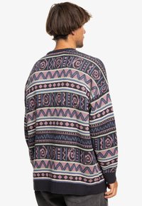 Patterned knit sweater featuring a dark base with pink, purple, and blue geometric designs and stripes. Ribbed cuffs and hem.