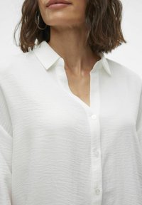 White button-up shirt featuring a textured fabric with a collar and a partial button placket, presenting a relaxed fit and soft drape.