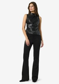 Crna, bezrukavna majica od sjajne kože s drapiranim dizajnom. Uparena s uskim crnim hlačama i cipelama s oštrom vrhom. Čist, minimalistički stil.