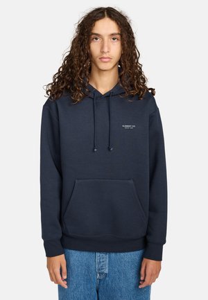 Marineblauwe hoodie gemaakt van zachte stof, met een voorzak in kangoeroestijl, trekkoorden en een klein logo op de borst.