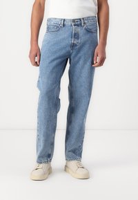 Jeanși de denim cu o nuanță albastră deschisă, cu o croială relaxată, design cu cinci buzunare și o textură ușor spălată. Purtați cu adidași de culoare crem.