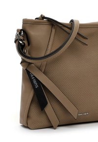 Beige perforated leather handbag with a zip closure, black strap accents, and a stylish tag. Features a soft texture and modern shape.