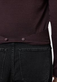 Burgundska pletena majica s rebrastim rubom i dva ljubičasta gumba straga, u kombinaciji s crnim trapericama koje imaju dva stražnja džepa.
