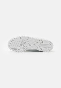 Vit idrottssko sula med strukturerad gummi för grepp, med ett geometriskt mönster och märkesdetaljer. Övergripande platt design för stabilitet.