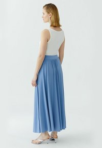 Lang blauwe rok met een vloeiende ontwerp en een geplooide taille, gecombineerd met een witte tanktop en zilveren sandalen met hakken. Soepele stoftextuur.
