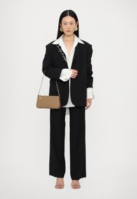 Blazer noir surdimensionné avec des détails brodés, chemise blanche et pantalon noir à jambes larges. Sac à main gris avec bandoulière en chaîne et sandales beiges.