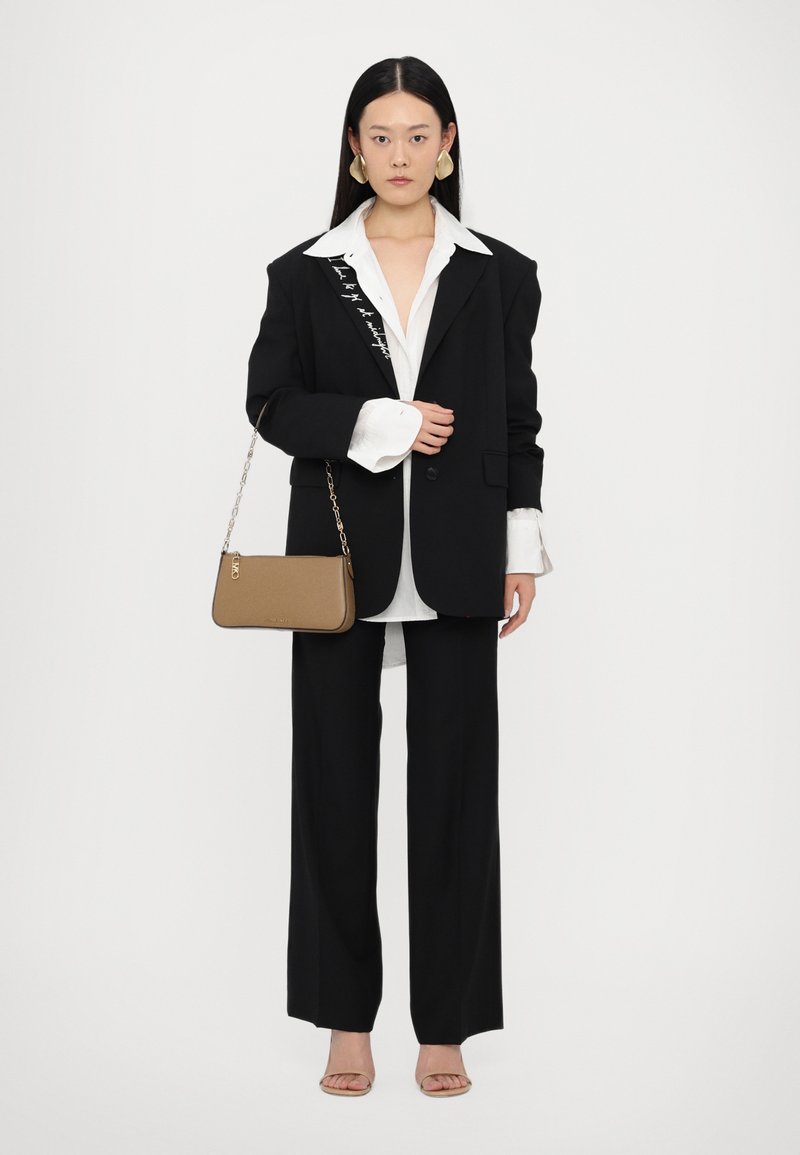 Blazer noir surdimensionné avec des détails brodés, chemise blanche et pantalon noir à jambes larges. Sac à main gris avec bandoulière en chaîne et sandales beiges.