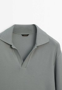 Szara koszulka polo z teksturowanej tkaniny, z kołnierzem z wycięciem i krótkimi rękawami, o wyraźnej konstrukcji, w klasycznym, casualowym stylu.