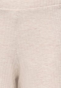 Close-up van beige geribbelde stof met subtiele verticale lijnen, waarbij de textuur en de details van het stikwerk worden benadrukt.