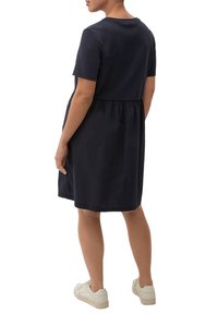 Robe en coton bleu marine à manches courtes, coupe ample et taille froncée. Portée avec des baskets de couleur claire, affichant un style décontracté.