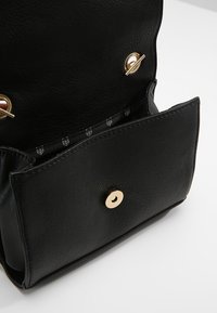Borsa in pelle nera aperta, con chiusura magnetica dorata e rivestimento interno in tessuto con motivo a piccoli elementi geometrici bianchi.