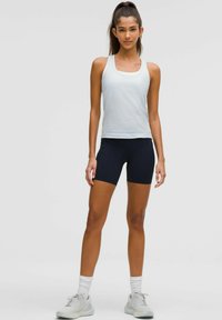 Lichtblauw tanktop en marineblauwe shorts van rekbaar materiaal. Model draagt grijze sportschoenen met witte sokken en staat op een lichte achtergrond.
