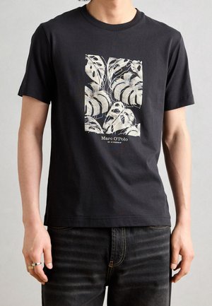 Czarny bawełniany t-shirt z białym wzorem liści na środku oraz nadrukiem nazwy marki "Marc O'Polo" poniżej. Krótkie rękawy.