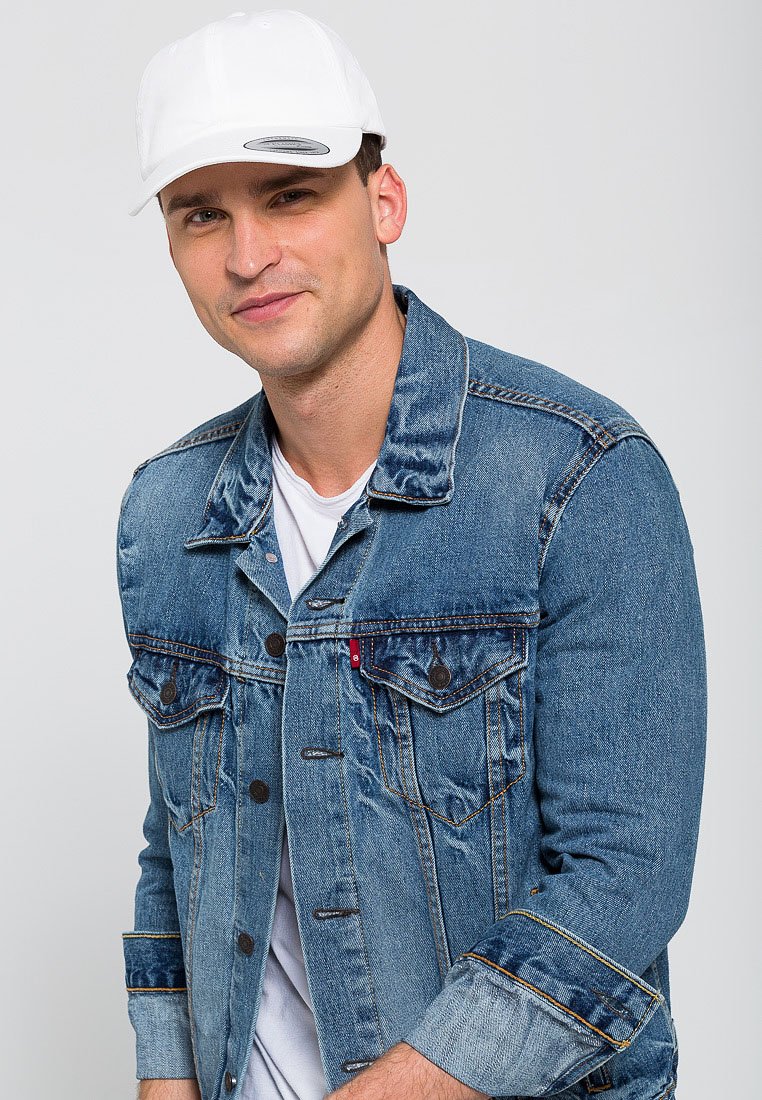 Lysblå denimjakke med klassisk skæring, der har to brystlommer og kontrasterende syninger. Bærer den over en hvid T-shirt og en hvid kasket.