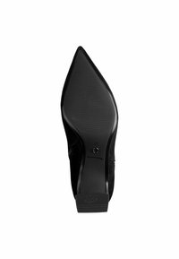 Chaussure à talon haut en suede noir avec un bout pointu. La semelle texturée présente des rainures verticales pour une meilleure adhérence. La marque est visible sur le talon.
