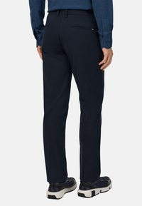 Granatowe spodnie wykonane z gładkiego materiału, z zamkiem błyskawicznym w tylnej kieszeni oraz dopasowanym krojem, w połączeniu z czarno-białymi butami sportowymi.