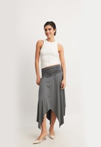 Hame grå, asymmetrisk med sammangruppad midja, i kombination med en åtsittande vit tanktopp och beige spetsiga klackar på en modell.