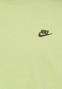 Ljusgrön tyg med en liten svart Nike-logga som har ordet och swoosh på den övre vänstra bröstområdet.