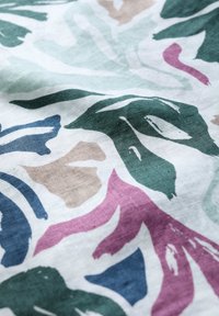 Tessuto con motivi a foglia in verde, blu, beige e rosa su uno sfondo bianco, con una finitura liscia e texture.