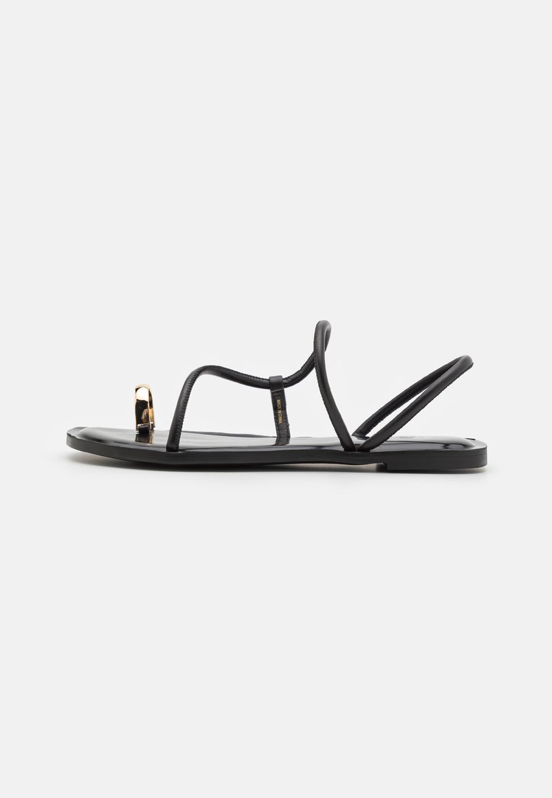 Svarta platta sandaler med tunna remmar och en tånring, med en guldaccent på tån. Tillverkade av ett slätt, glänsande material.